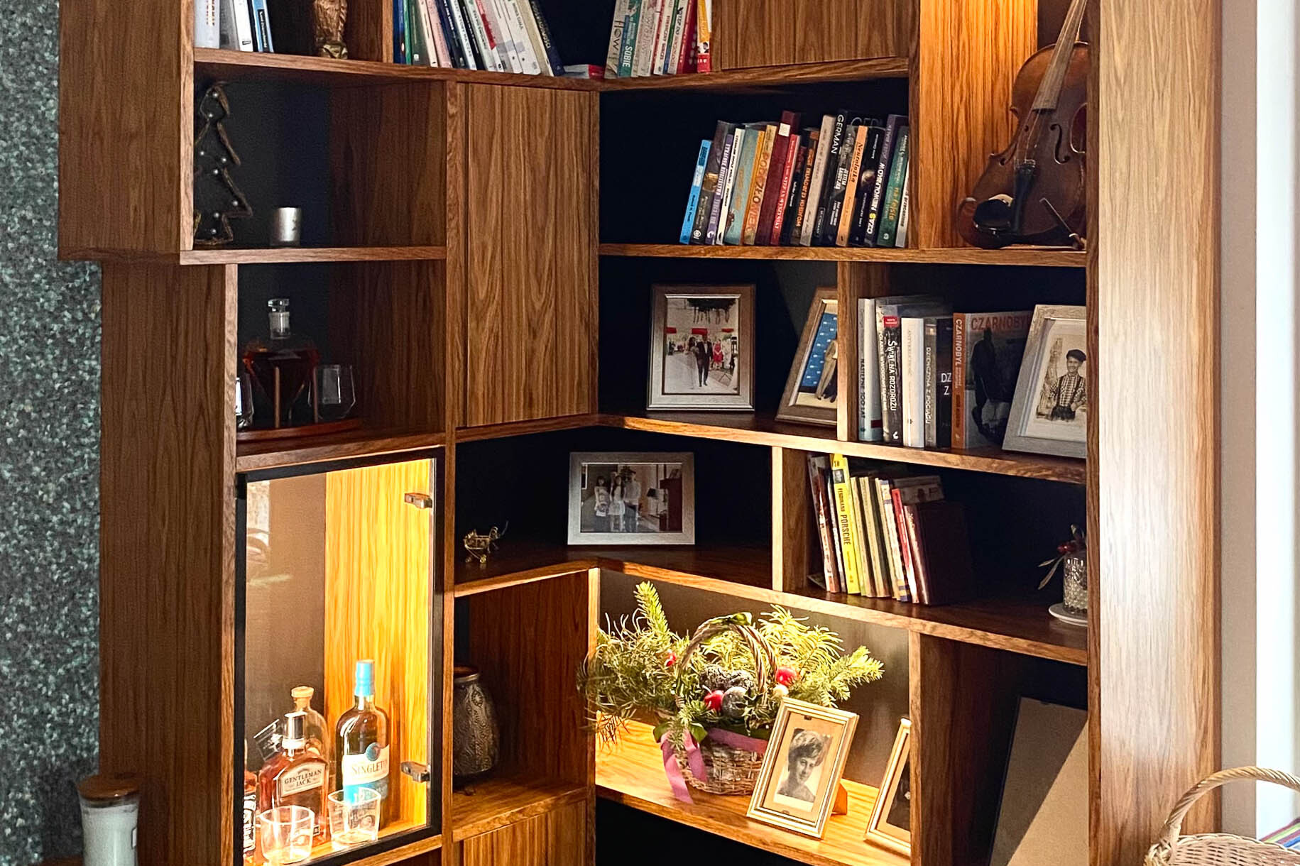 narożnik biblioteczki z wyeksponowanymi przedmiotami: książkami, świecami, skrzypcami oraz przeszkloną gablotką na alkohol