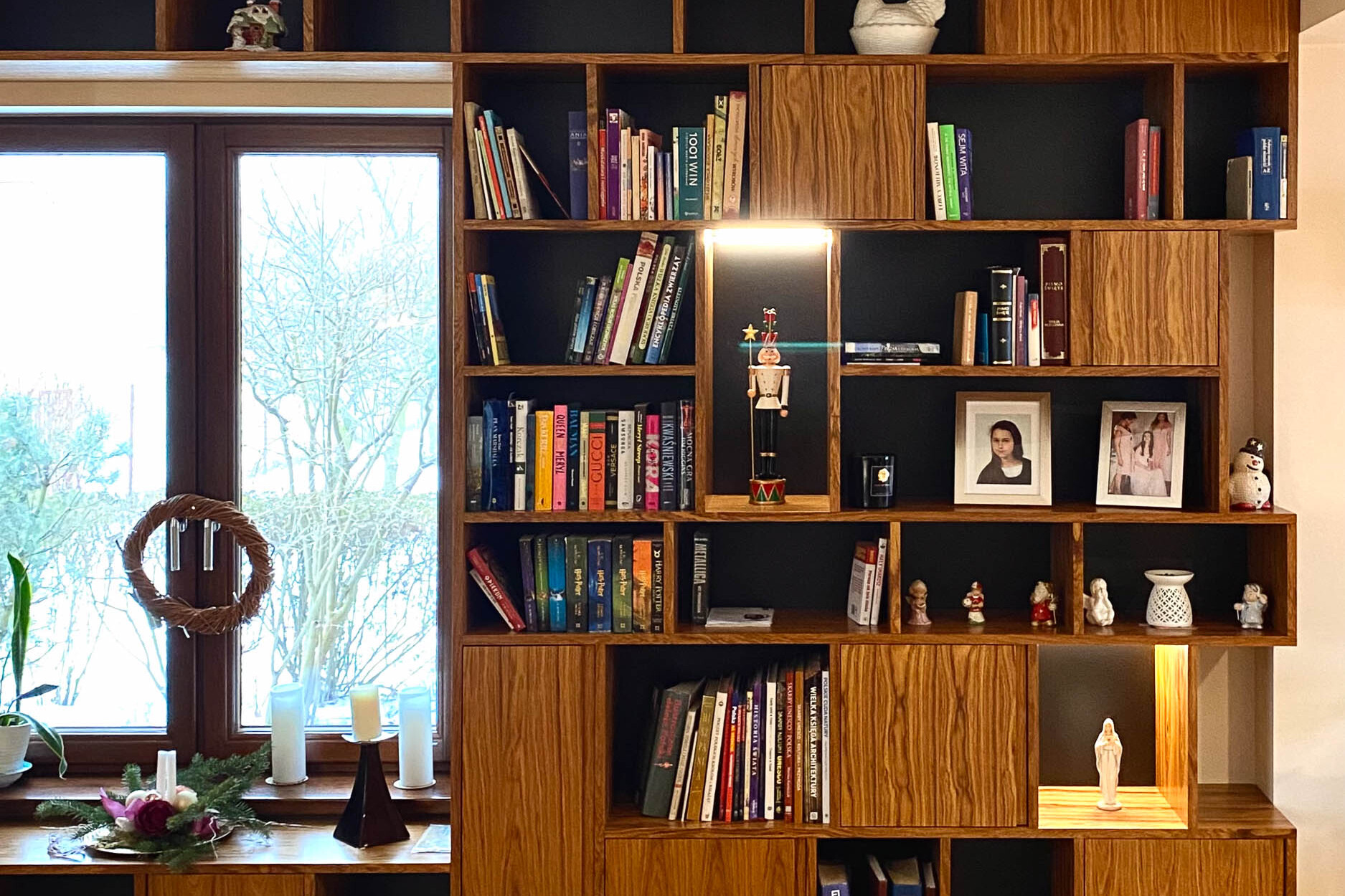 biblioteczka z wyeksponowanymi przedmiotami: książkami, zdjęciami w ramkach, figurkami i porcelaną