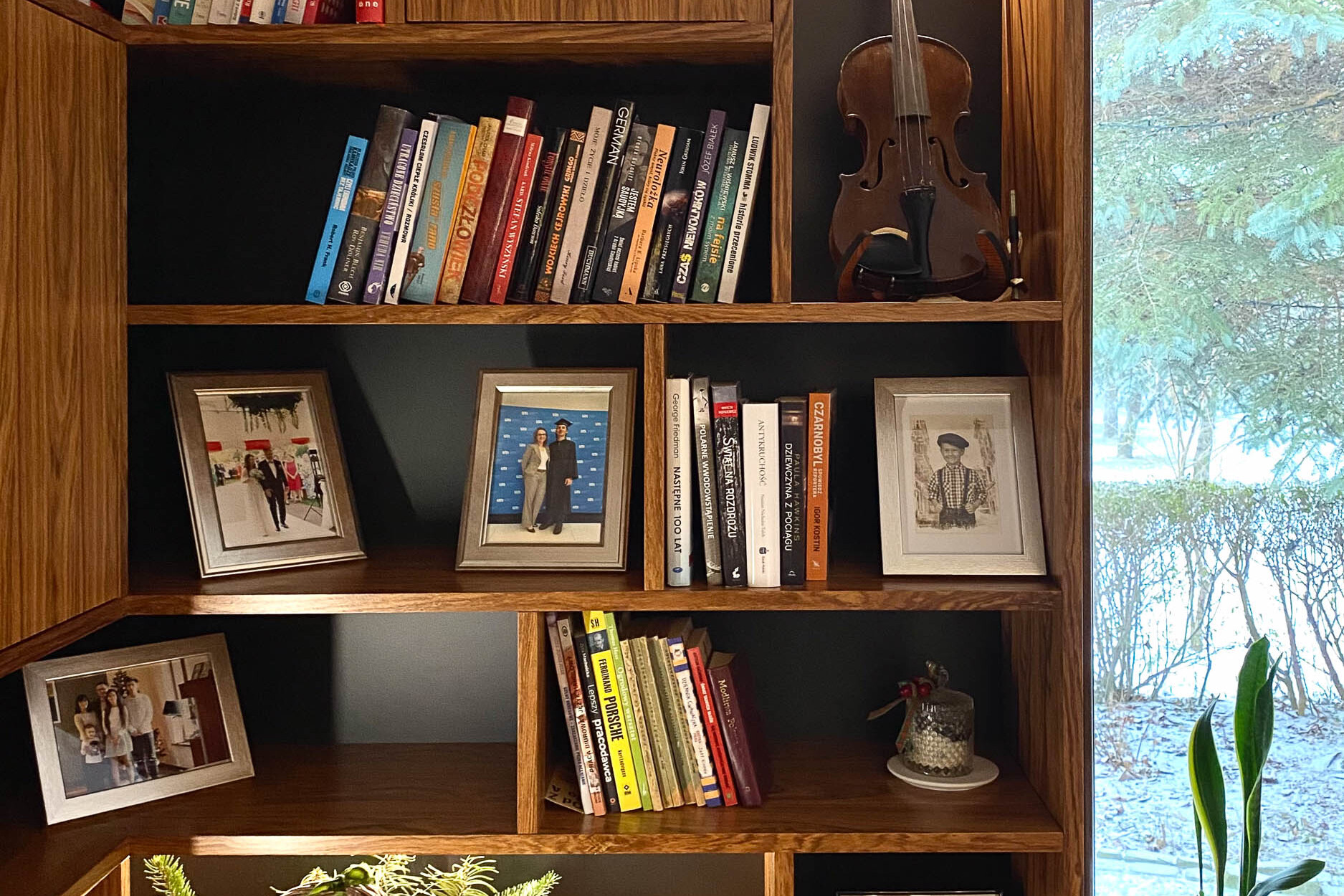 biblioteczka - regał, na którym wyeksponowane są osobiste przedmioty takie jak książki, ramki ze zdjęciami, skrzypce i stroiki