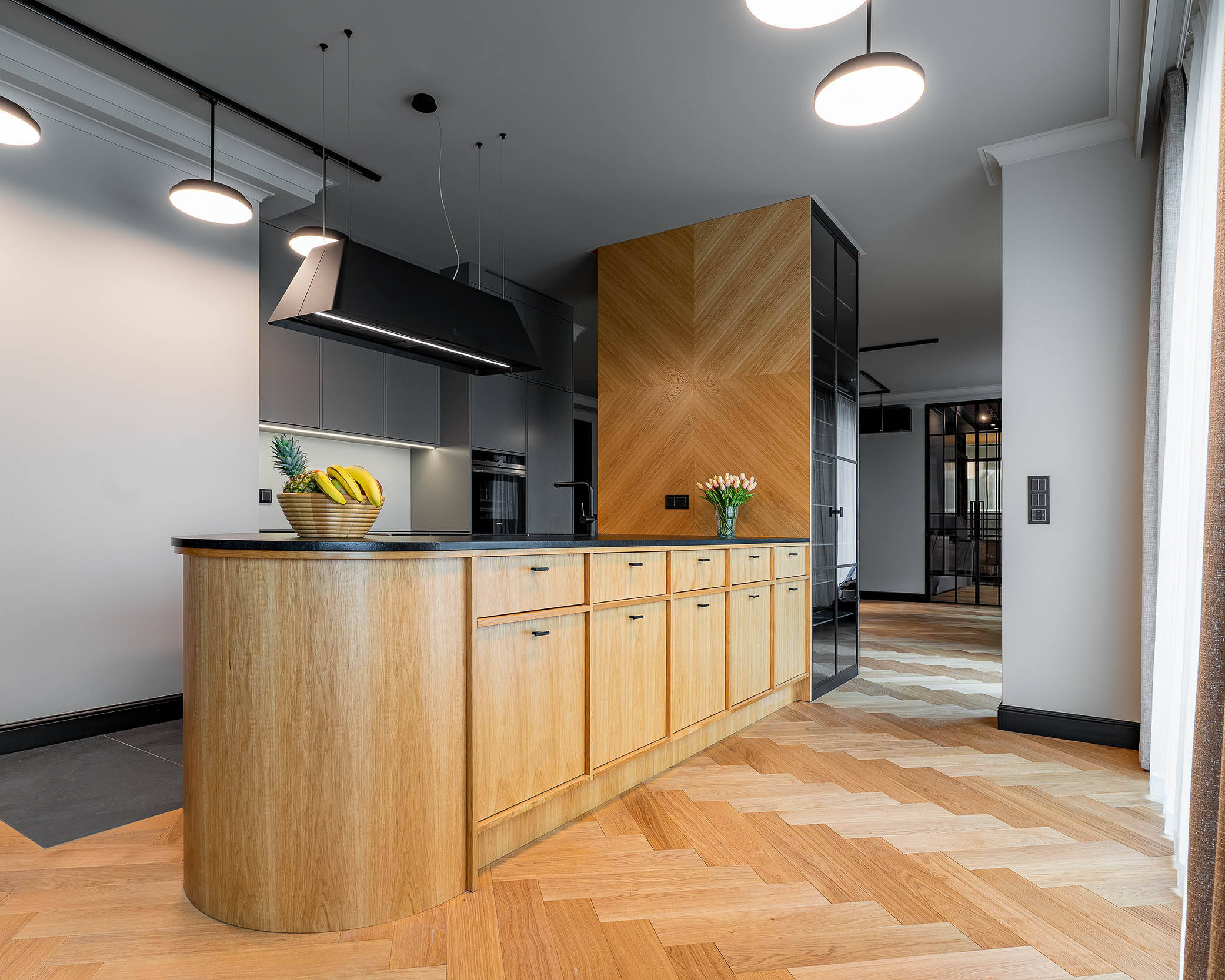 kuchnia w apartamencie z forniru w kolorze naturalnego dębu polskiego, na środku kuchni półwysep, nad p;ółwyspem designerski czarny okap z oświetleniem